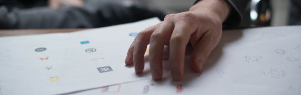 Une main examine plusieurs propositions de logos imprimées sur des feuilles de papier