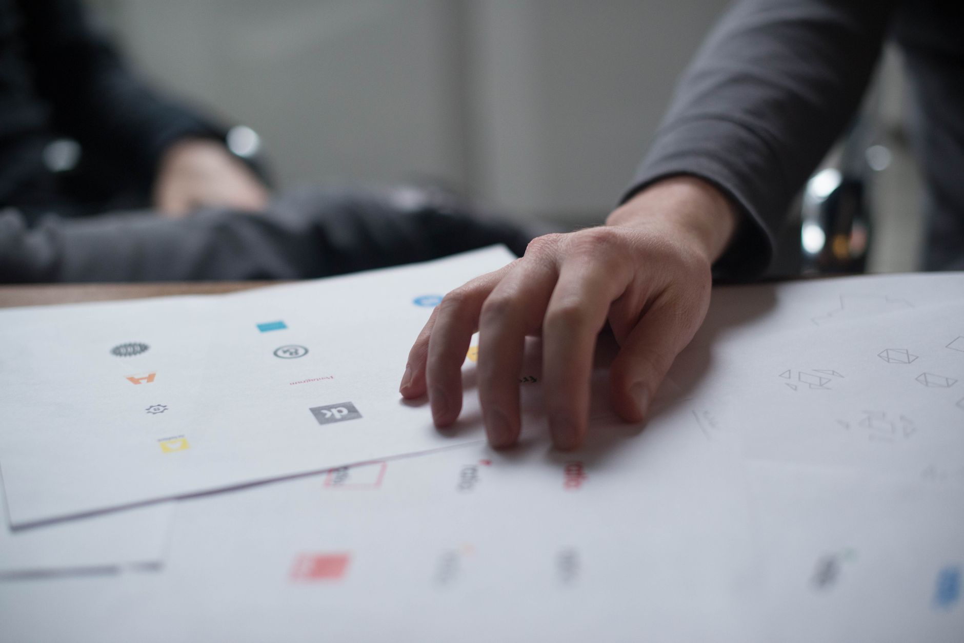 Une main examine plusieurs propositions de logos imprimées sur des feuilles de papier