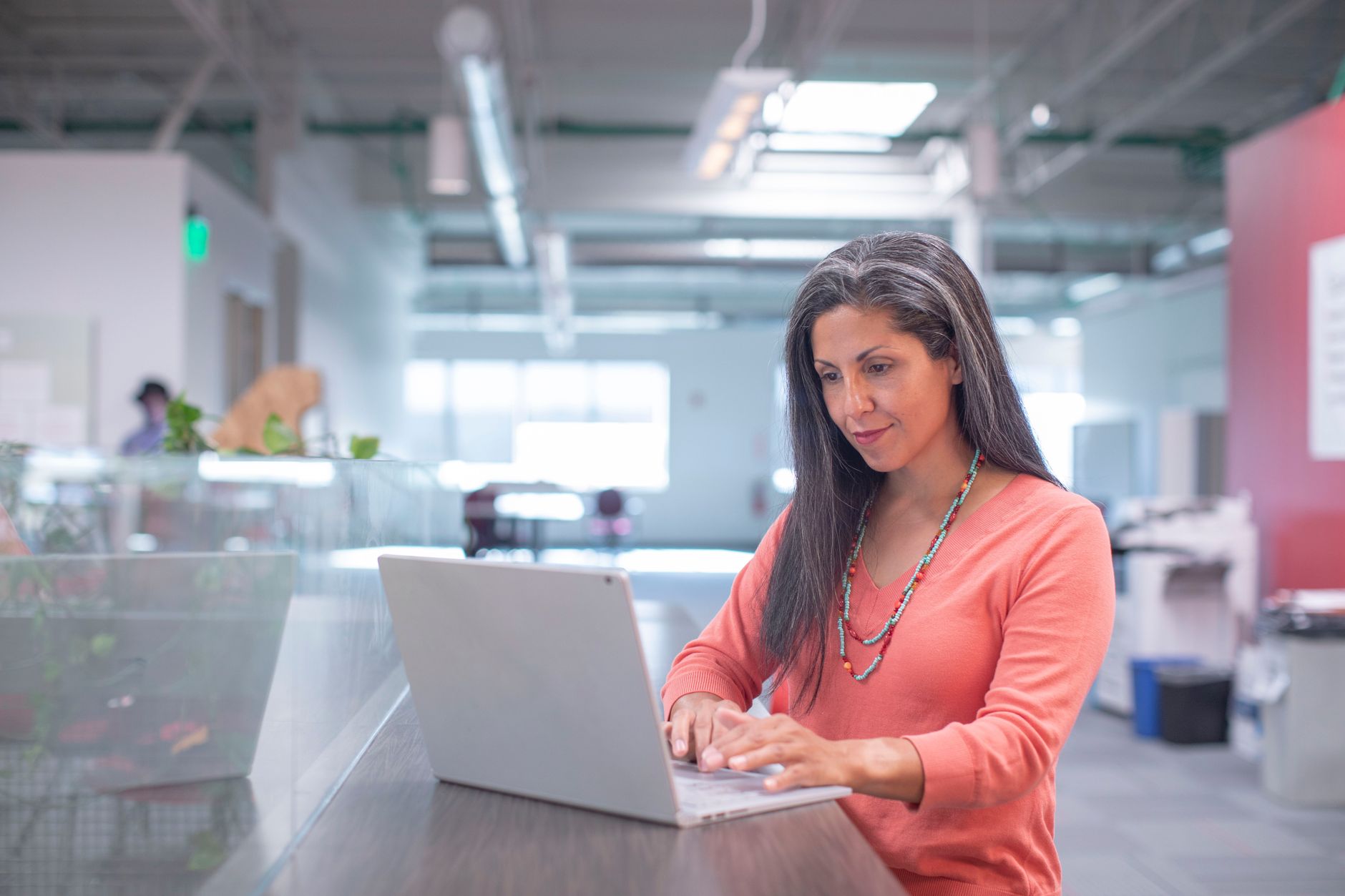 Femme en haut rose qui tape sur un ordinateur portable dans un bureau lumineux, en pleine recherche en ligne