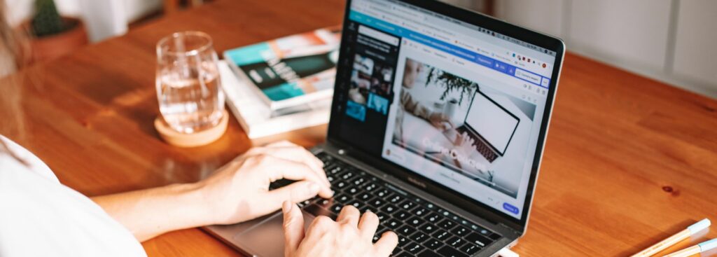 Personne qui travaille sur un ordinateur portable à un bureau en bois, avec un carnet et des stylos à côté