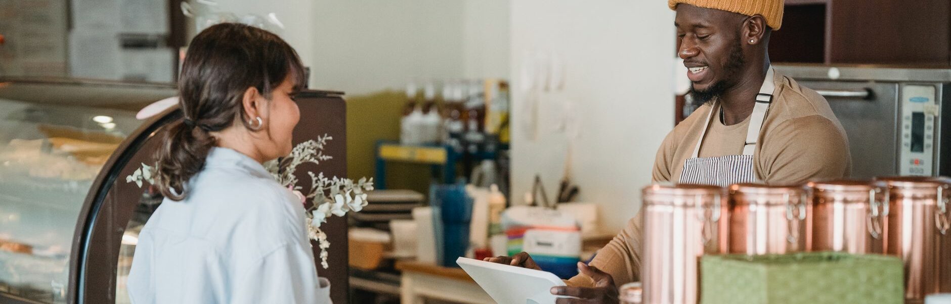 Une barista et une cliente échangent avec le sourire au comptoir d’un café, ambiance chaleureuse