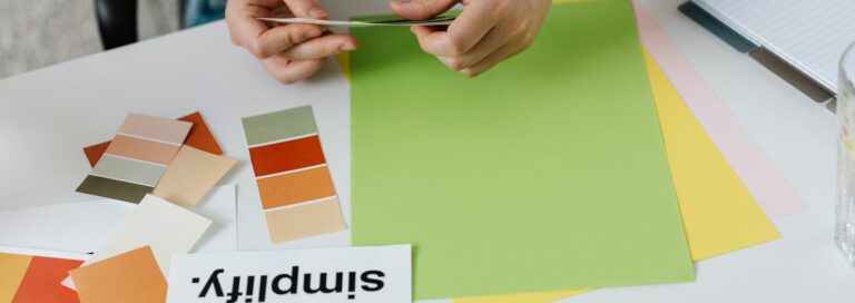 Une personne dispose des nuanciers et échantillons de papier colorés sur un bureau pour composer une palette de couleurs