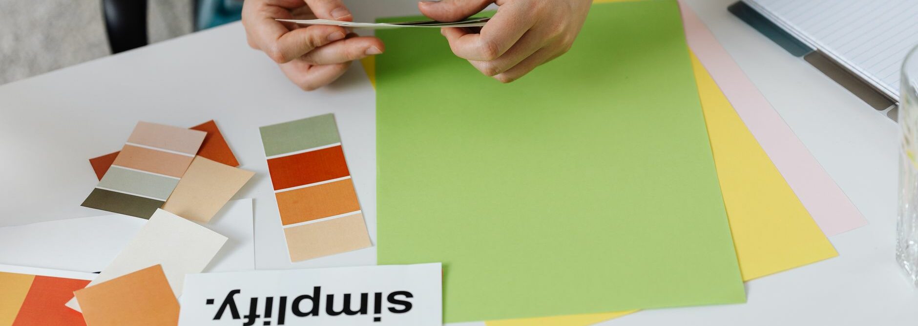 Une personne dispose des nuanciers et échantillons de papier colorés sur un bureau pour composer une palette de couleurs