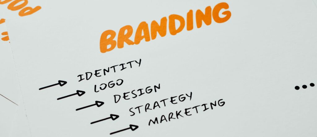 Feuille posée sur un bureau où sont écrits en orange et noir les mots branding, identité, design, stratégie et marketing