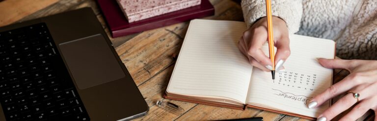 Une femme planifie son calendrier dans un carnet à côté d’un ordinateur portable sur un bureau en bois