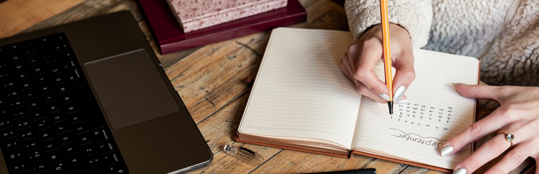 Une femme planifie son calendrier dans un carnet à côté d’un ordinateur portable sur un bureau en bois