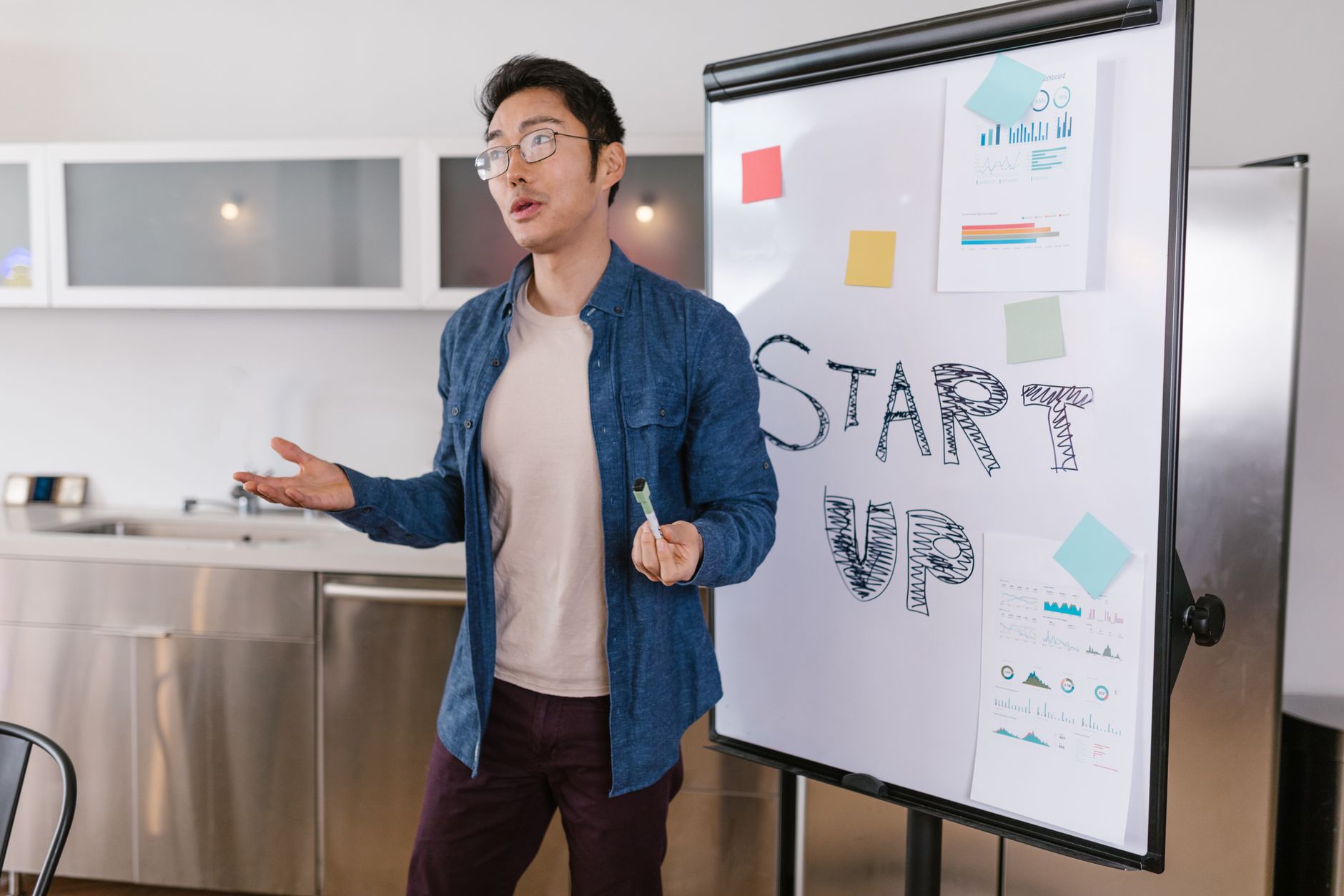 Homme debout devant un tableau blanc couvert de schémas, en train de présenter un plan de lancement à une équipe