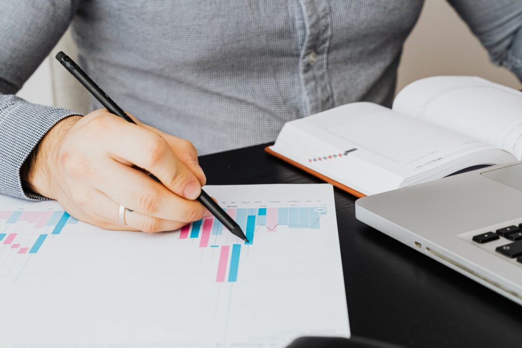 Une personne examine un graphique sur une feuille, avec un ordinateur portable et un carnet posés sur le bureau