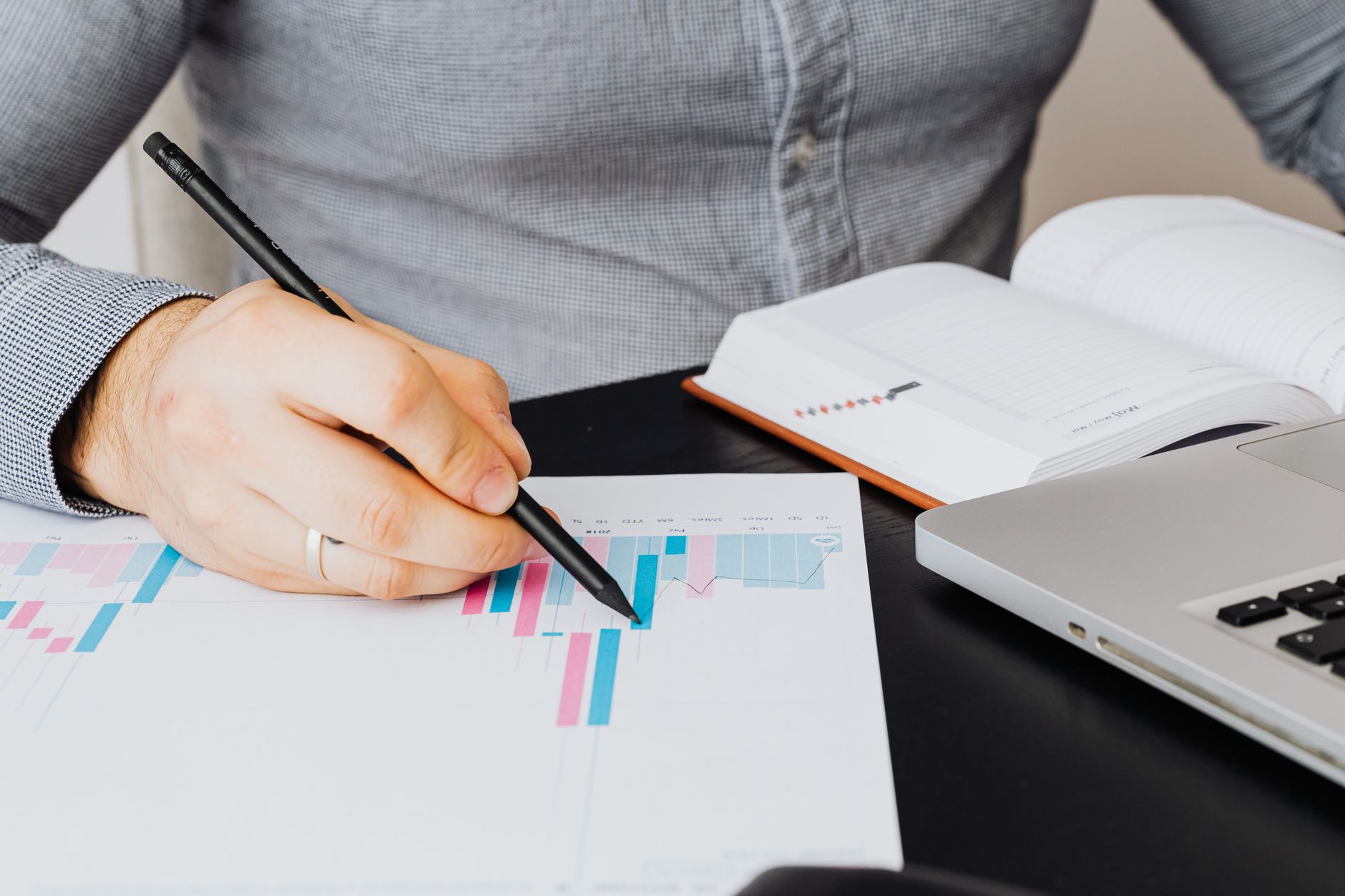 Une personne examine un graphique sur une feuille, avec un ordinateur portable et un carnet posés sur le bureau