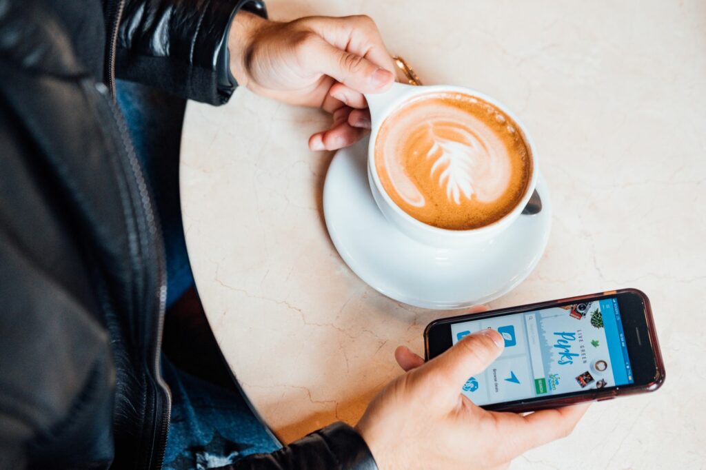 Personne qui consulte un site web sur son smartphone en tenant un café latte